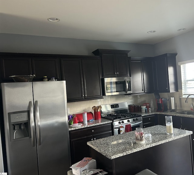 kitchen with sink, tasteful backsplash, light stone counters, a kitchen island, and stainless steel appliances