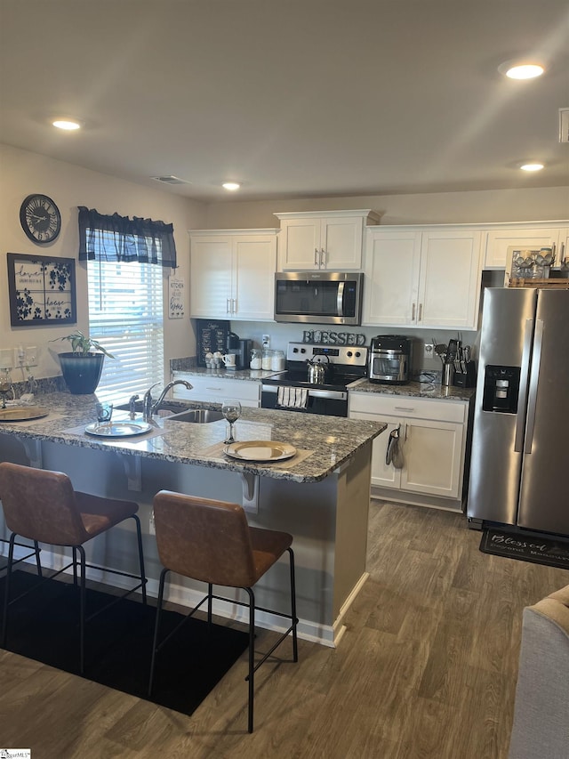 kitchen featuring stone counters, white cabinetry, dark hardwood / wood-style flooring, a kitchen breakfast bar, and stainless steel appliances