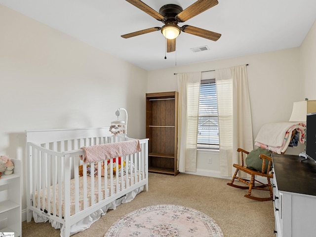 bedroom with ceiling fan, light colored carpet, and a crib