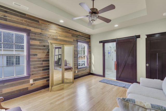 living room with a raised ceiling, a barn door, wooden walls, and light hardwood / wood-style flooring