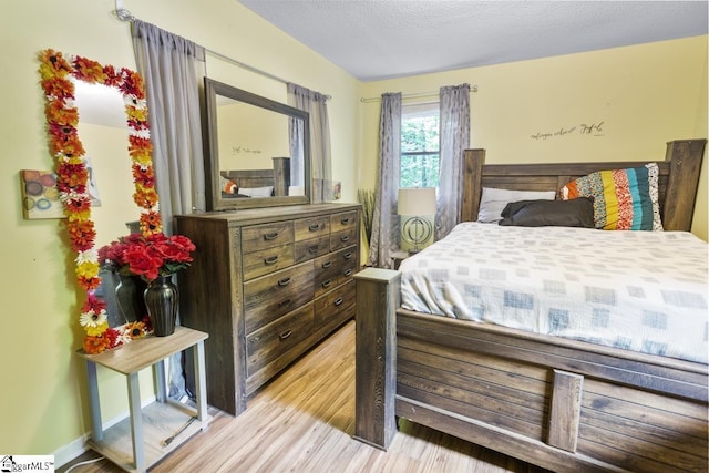 bedroom featuring vaulted ceiling, light hardwood / wood-style flooring, and a textured ceiling