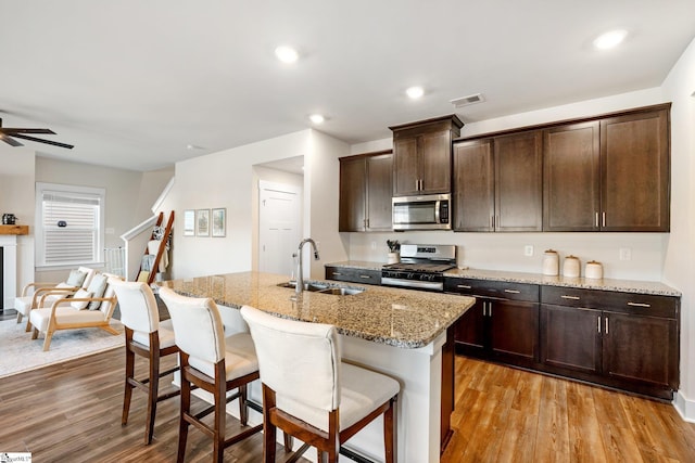 kitchen with sink, light hardwood / wood-style flooring, an island with sink, stainless steel appliances, and light stone countertops