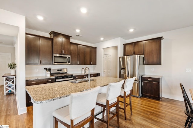 kitchen featuring sink, a kitchen island with sink, stainless steel appliances, a kitchen breakfast bar, and light stone counters