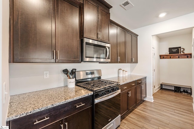 kitchen featuring light stone countertops, dark brown cabinets, stainless steel appliances, and light wood-type flooring