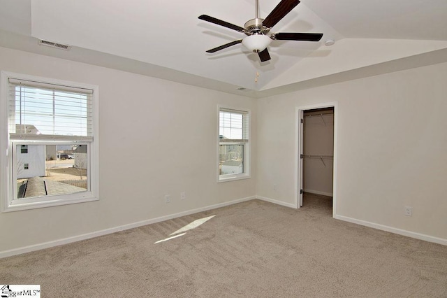 unfurnished bedroom with ceiling fan, vaulted ceiling, a walk in closet, light colored carpet, and a closet