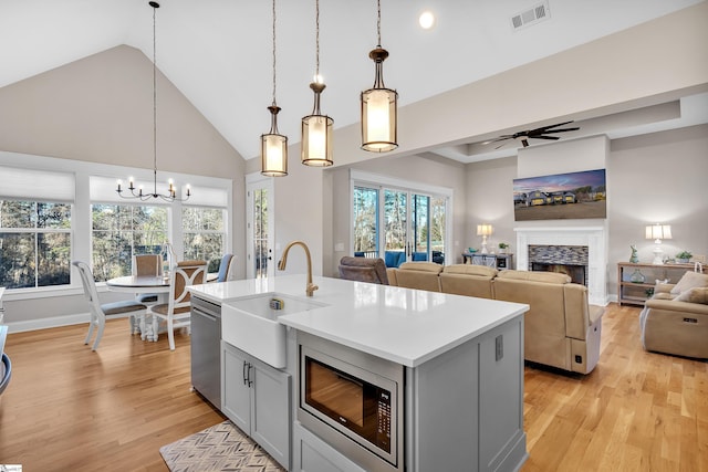 kitchen featuring sink, decorative light fixtures, a center island with sink, stainless steel appliances, and ceiling fan with notable chandelier