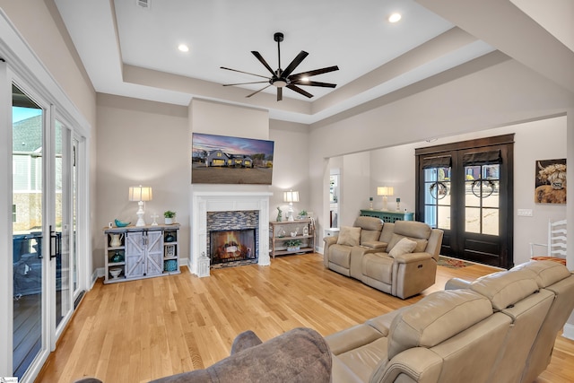 living room with a tray ceiling, light hardwood / wood-style floors, french doors, and a tile fireplace