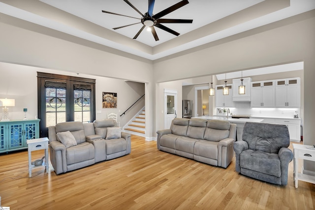 living room with sink, a high ceiling, ceiling fan, a tray ceiling, and light hardwood / wood-style flooring