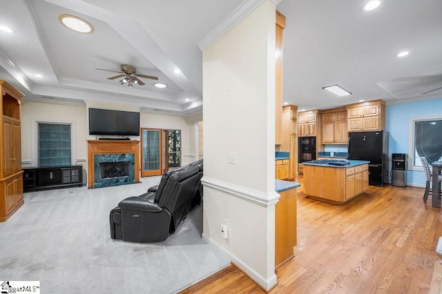 kitchen featuring a kitchen island, black appliances, crown molding, a tray ceiling, and a premium fireplace