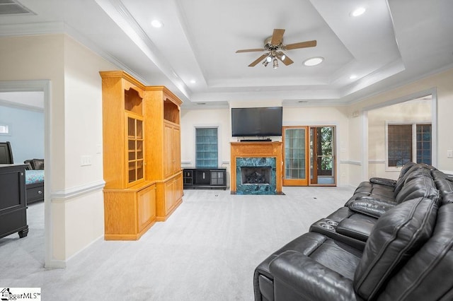 carpeted living room with a premium fireplace, crown molding, a raised ceiling, and ceiling fan