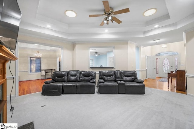 carpeted living room featuring crown molding, a tray ceiling, and ceiling fan with notable chandelier