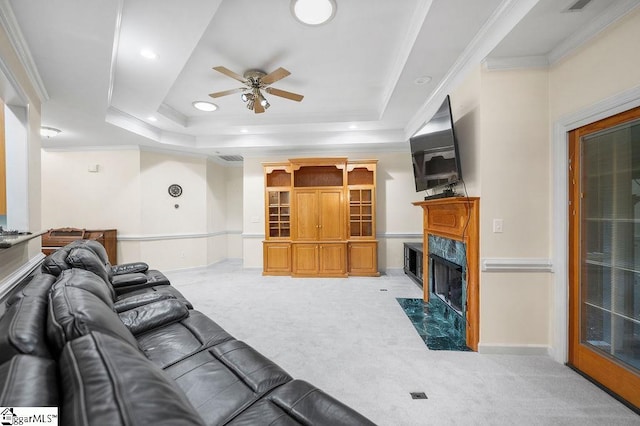 living room featuring light colored carpet, ornamental molding, a tray ceiling, and a fireplace