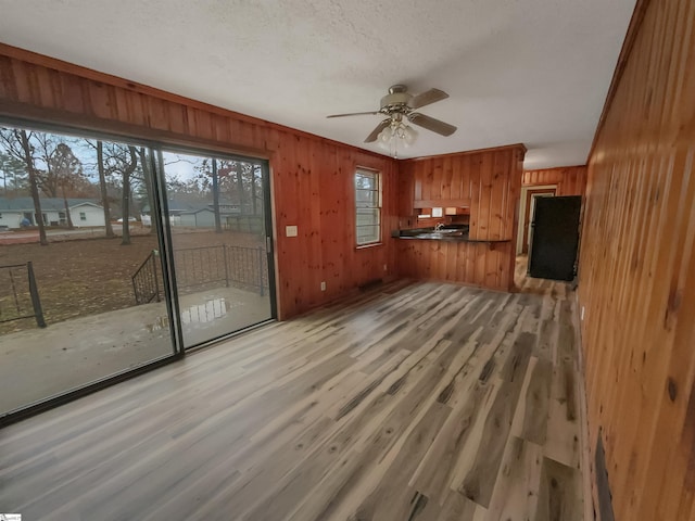 unfurnished living room featuring ceiling fan, wood walls, a textured ceiling, and light hardwood / wood-style flooring