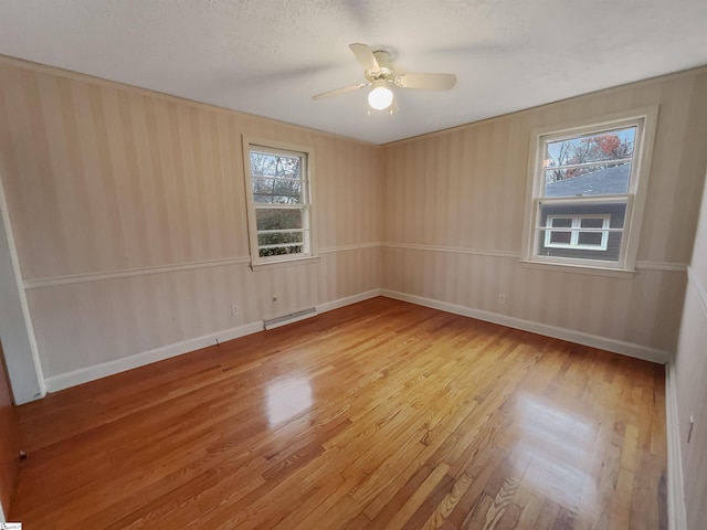 empty room featuring baseboard heating, ceiling fan, wood-type flooring, and a textured ceiling