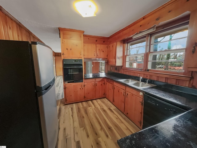 kitchen with sink, light hardwood / wood-style flooring, wooden walls, and black appliances