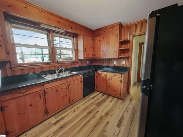 kitchen featuring stainless steel refrigerator, wood walls, black dishwasher, sink, and light hardwood / wood-style floors