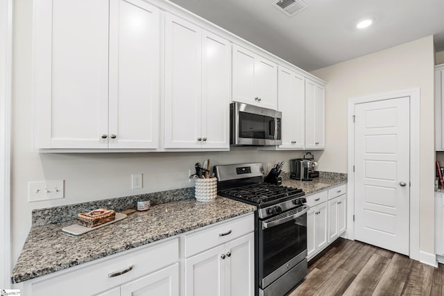 kitchen with stainless steel appliances, white cabinetry, light stone countertops, and dark hardwood / wood-style flooring