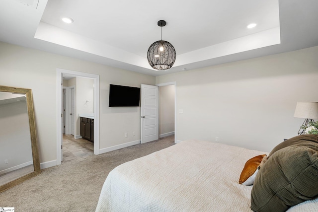 bedroom featuring ensuite bathroom, light carpet, and a tray ceiling