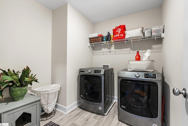 clothes washing area with washing machine and clothes dryer and light wood-type flooring