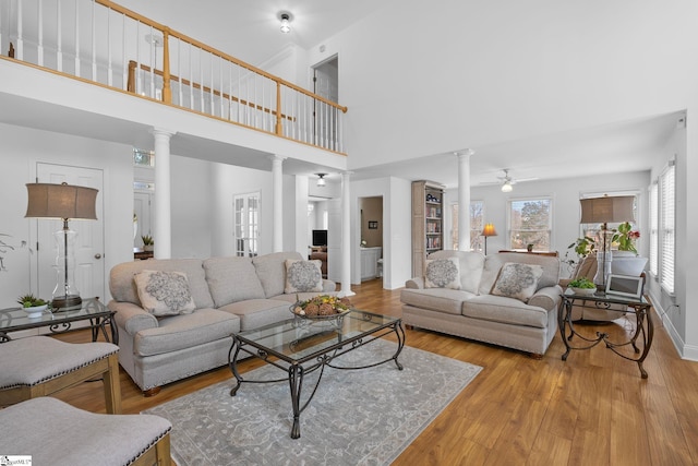 living room with ornate columns, a high ceiling, ceiling fan, and light hardwood / wood-style flooring