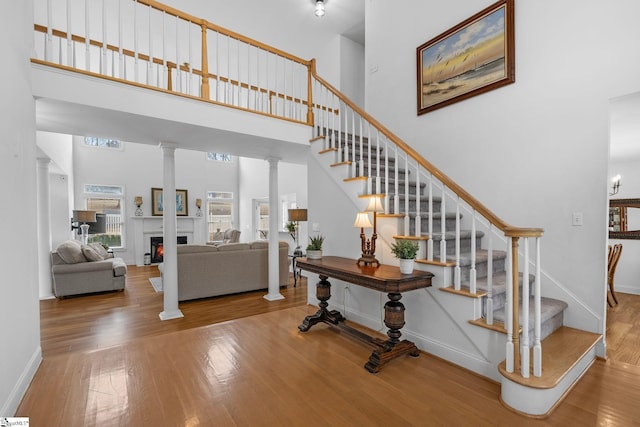 stairs with a high ceiling, wood-type flooring, and decorative columns