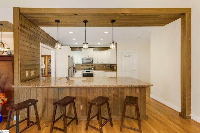 kitchen with white cabinetry, kitchen peninsula, pendant lighting, stainless steel appliances, and light stone countertops