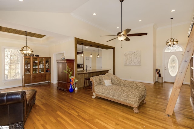 living room featuring ceiling fan with notable chandelier, wood-type flooring, ornamental molding, and vaulted ceiling