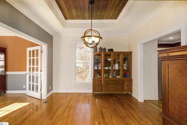 unfurnished dining area with ornamental molding, hardwood / wood-style floors, an inviting chandelier, and a tray ceiling