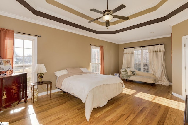 bedroom with crown molding, light wood-type flooring, ceiling fan, and a tray ceiling