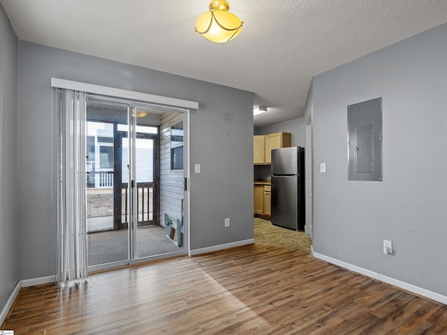 unfurnished room with a textured ceiling, electric panel, and light hardwood / wood-style floors