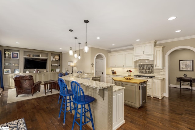 kitchen with pendant lighting, sink, a kitchen island with sink, light stone counters, and ornamental molding