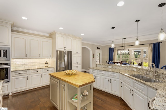 kitchen featuring appliances with stainless steel finishes, butcher block countertops, sink, decorative backsplash, and a center island