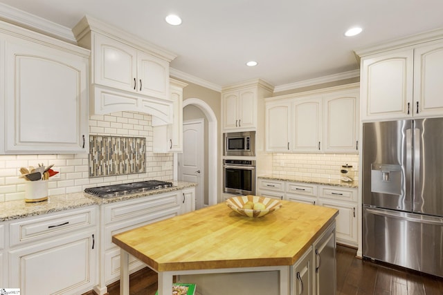 kitchen featuring a kitchen island, butcher block countertops, tasteful backsplash, stainless steel appliances, and crown molding