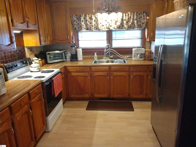 kitchen with electric stove, sink, stainless steel fridge, light hardwood / wood-style flooring, and decorative light fixtures