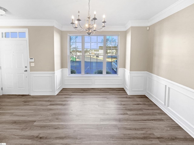 unfurnished dining area featuring crown molding, hardwood / wood-style flooring, and a notable chandelier