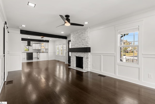 unfurnished living room with ceiling fan, hardwood / wood-style floors, beam ceiling, a stone fireplace, and a barn door