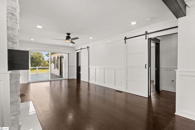 unfurnished living room featuring dark hardwood / wood-style floors, ornamental molding, a barn door, and ceiling fan