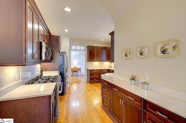 kitchen with tasteful backsplash, crown molding, light stone counters, light wood-type flooring, and appliances with stainless steel finishes