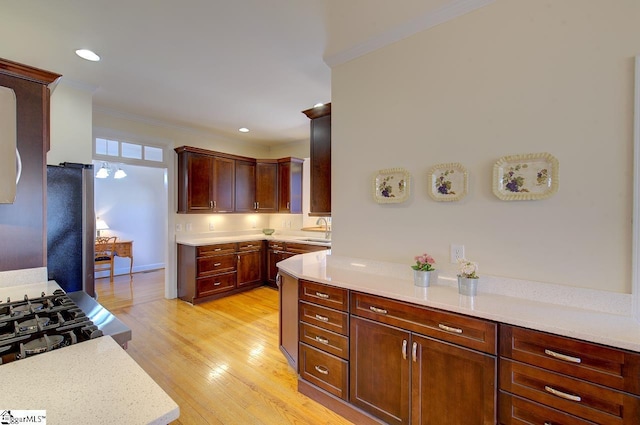 kitchen featuring sink, stainless steel fridge, light stone counters, light hardwood / wood-style floors, and ornamental molding