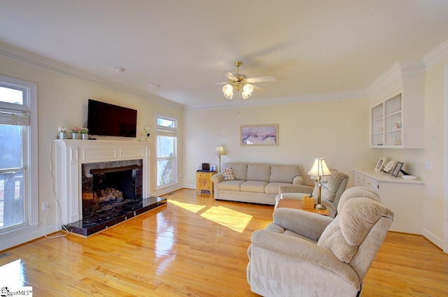 living room featuring crown molding, ceiling fan, a high end fireplace, and light hardwood / wood-style flooring