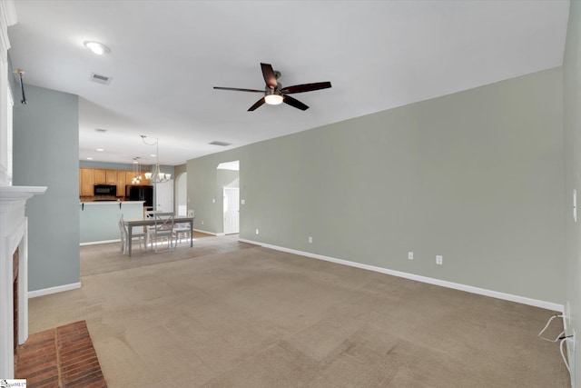 unfurnished living room with a brick fireplace, ceiling fan with notable chandelier, and light carpet