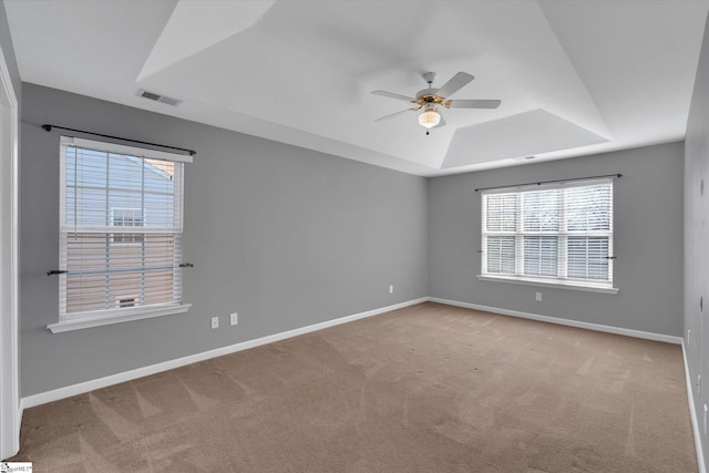 carpeted empty room with a raised ceiling, a wealth of natural light, and ceiling fan