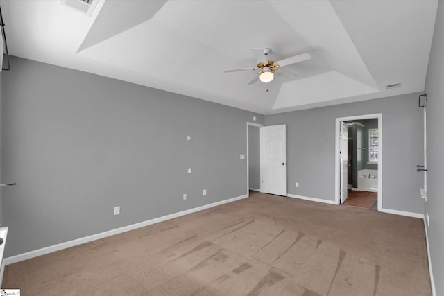 unfurnished bedroom with ceiling fan, ensuite bathroom, carpet flooring, and a raised ceiling