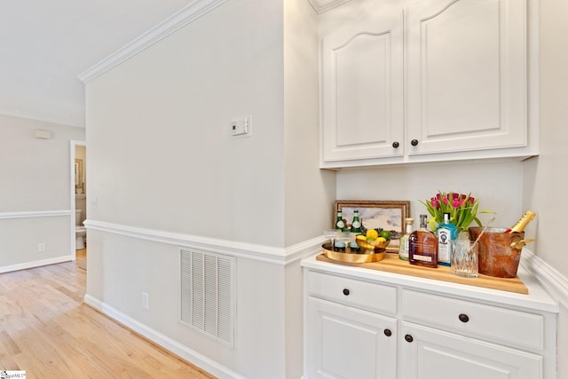 bar featuring white cabinetry, ornamental molding, and light wood-type flooring