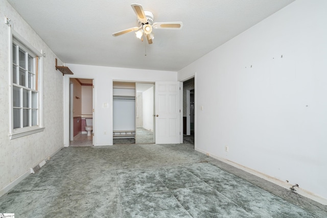 unfurnished bedroom with ceiling fan, ensuite bath, and a textured ceiling