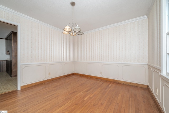 empty room featuring crown molding, light hardwood / wood-style floors, and a chandelier