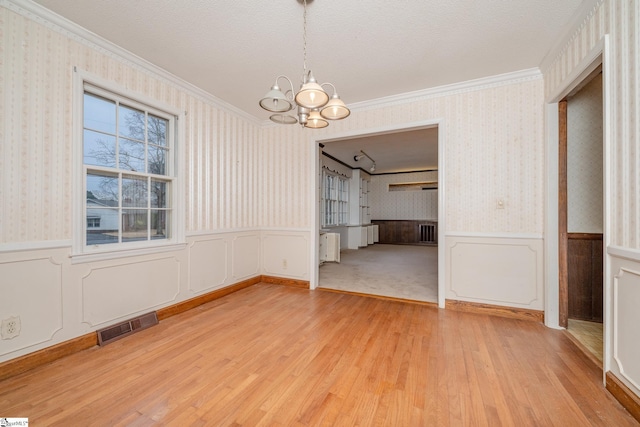 unfurnished dining area featuring ornamental molding, a chandelier, a textured ceiling, and light wood-type flooring