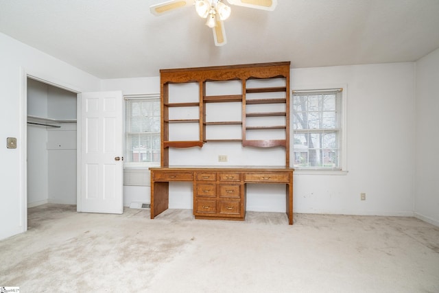 unfurnished office featuring built in desk, light carpet, and ceiling fan