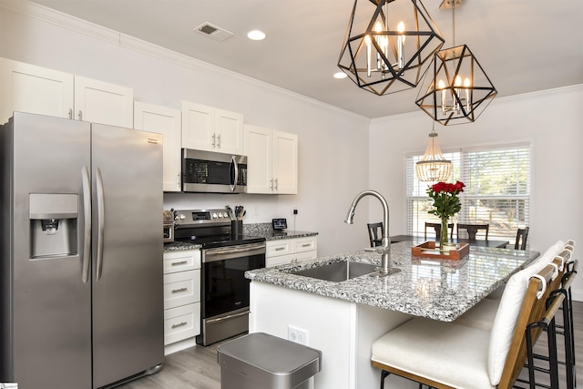 kitchen with sink, white cabinetry, decorative light fixtures, appliances with stainless steel finishes, and a kitchen island with sink