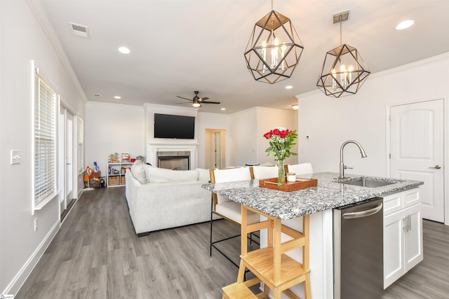 kitchen with sink, white cabinets, hanging light fixtures, light stone countertops, and a center island with sink